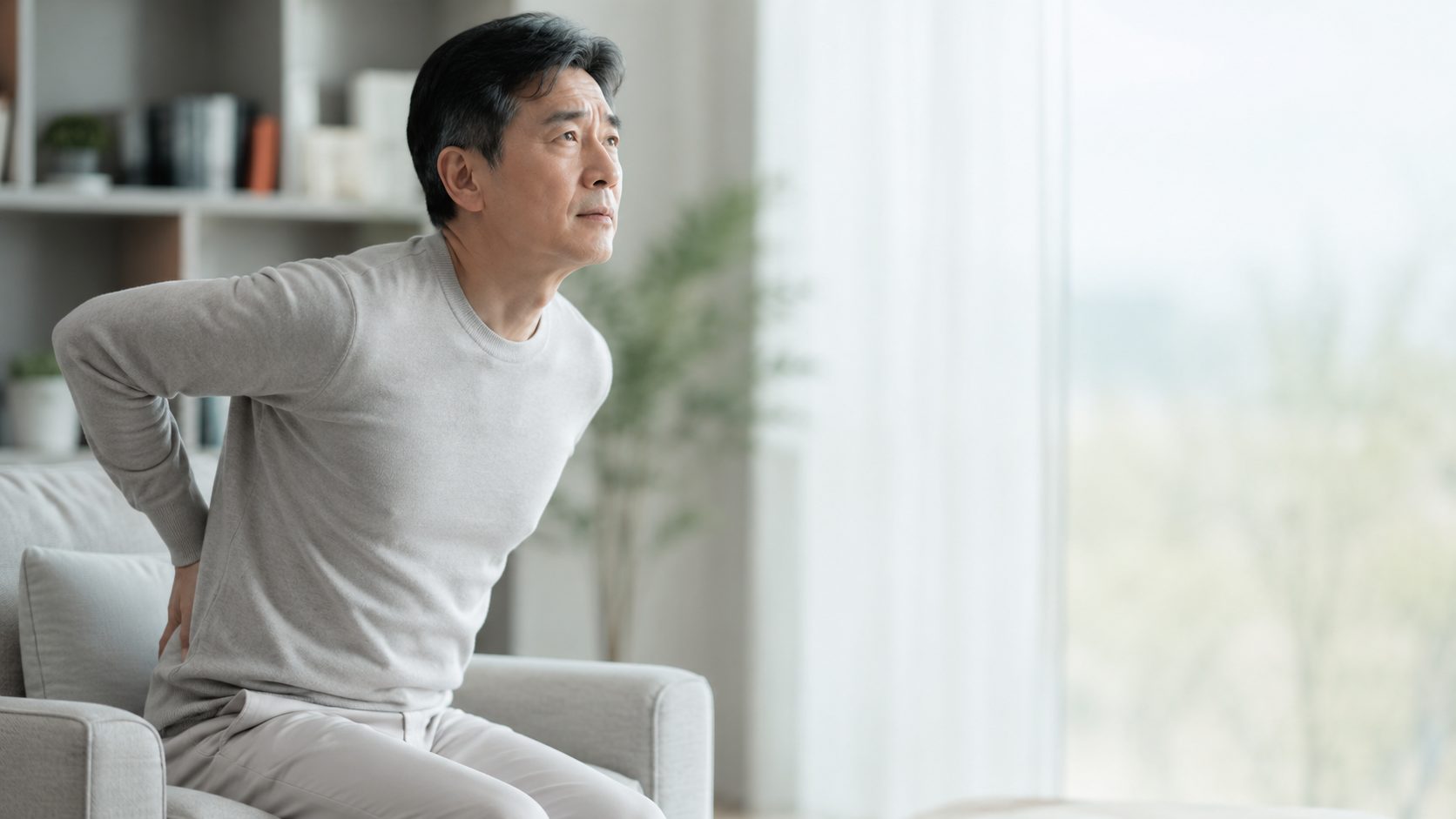 소파에서 천천히 일어나며 허리에 가벼운 불편감을 느끼는 중년 남성